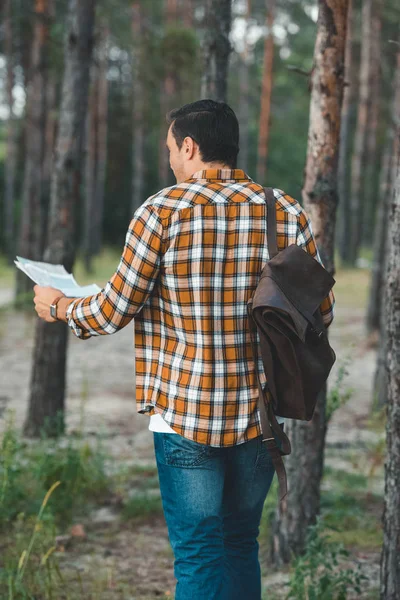 Vista trasera de turista con mapa y mochila en bosque - foto de stock