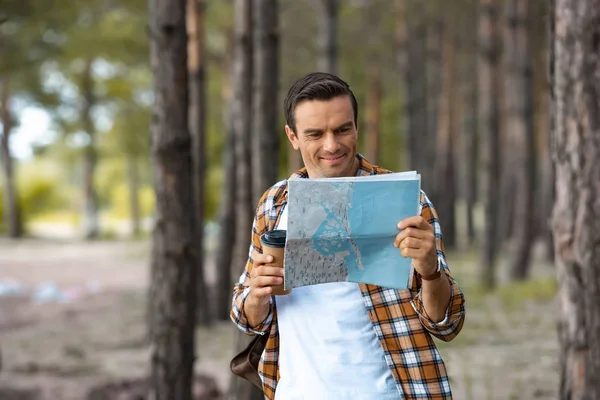 Retrato de turista sonriente con mapa y café para ir en el bosque - foto de stock
