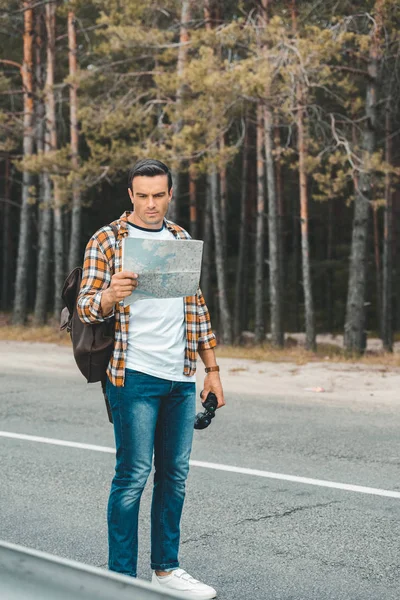 Tourist with binoculars looking at map while standing on empty road — Stock Photo