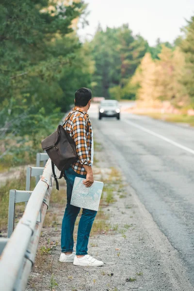 Vue latérale de l'homme avec sac à dos et carte debout sur la route tout en voyageant seul — Photo de stock