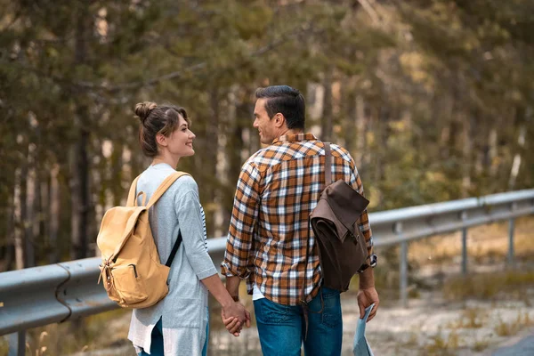 Back view of tourists with backpacks holding hands while walking on road together — Stock Photo