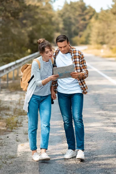 Turistas con mapa en busca de destino, mientras que de pie en el camino vacío - foto de stock