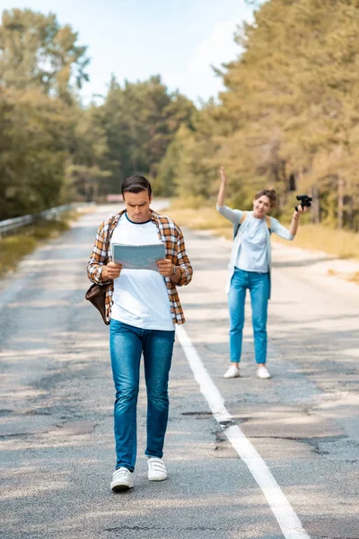 Selective focus of man with map and girlfriend with binoculars behind on road — Stock Photo