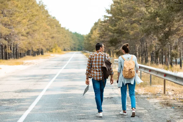 Back view of tourists with backpacks walking on empty road — Stock Photo