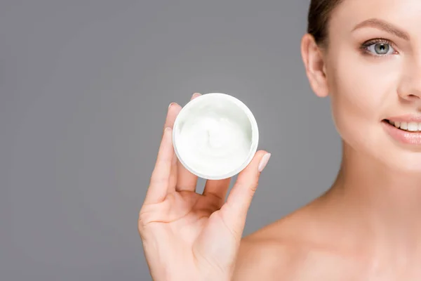 Cropped shot of smiling woman holding face cream in jar isolated on grey — Stock Photo