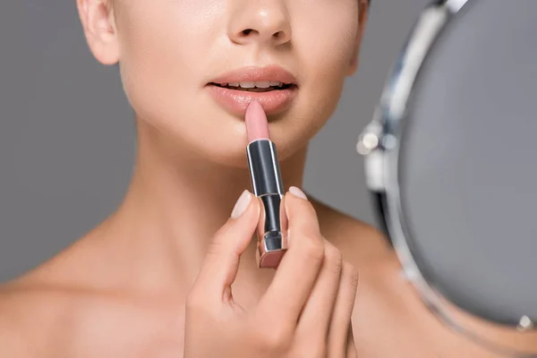 Cropped shot of woman with mirror applying nude lipstick isolated on grey — Stock Photo