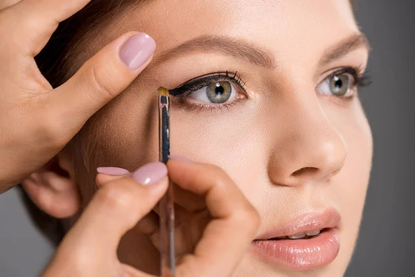 Cropped shot of makeup artist applying eyeliner on models face on grey backdrop — Stock Photo
