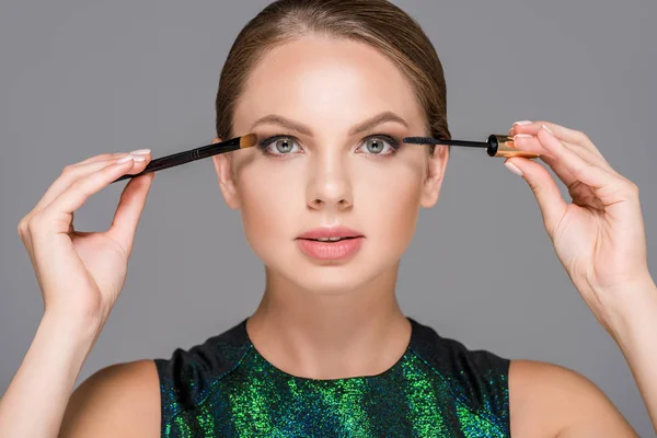 Retrato de mujer elegante con rímel y pincel de maquillaje para sombras de ojos aislados en gris - foto de stock