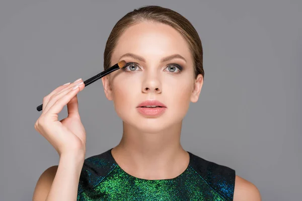 Porträt einer eleganten Frau mit Make-up-Pinsel für Lidschatten isoliert auf grau — Stockfoto
