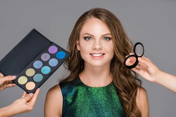 Partial view of makeup artists with cosmetics and smiling woman isolated on grey — Stock Photo
