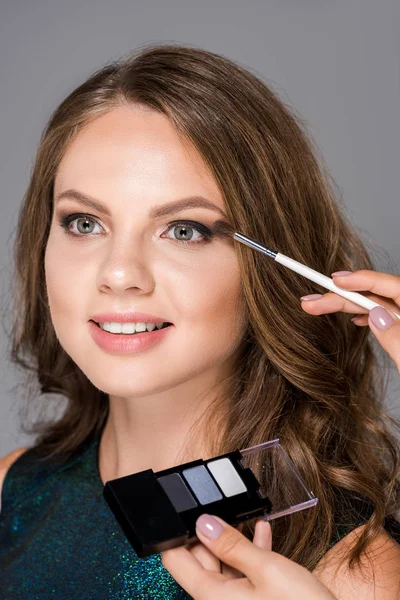 Cropped shot of makeup artist applying eyeshadows on models face isolated on grey — Stock Photo