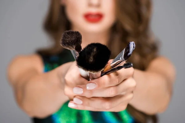 Vue partielle de la femme montrant des pinceaux de maquillage dans les mains sur fond gris — Photo de stock