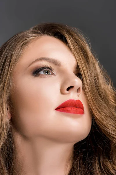 Retrato de mujer hermosa con lápiz labial rojo en los labios mirando hacia otro lado aislado en gris - foto de stock