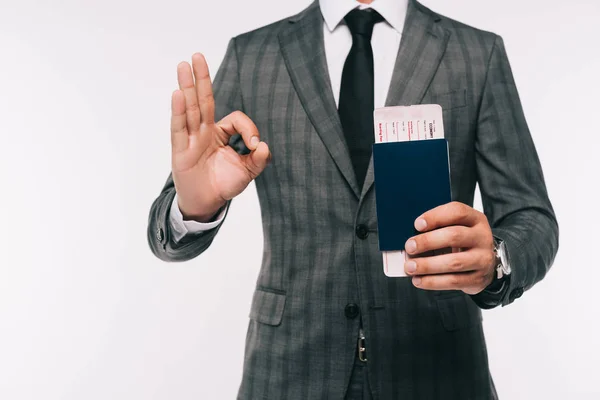 Обрізане зображення бізнесмена, який тримає паспорт і квиток і показує нормальний жест ізольовано на білому — стокове фото