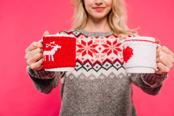 Cropped image of girl in sweater showing two different cups isolated on pink — Stock Photo