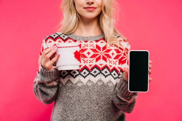 Cropped image of girl in sweater holding cup and smartphone with blank screen isolated on pink — Stock Photo