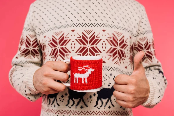 Cropped image of man in sweater holding cup with deer silhouette and showing thumb up isolated on pink — Stock Photo