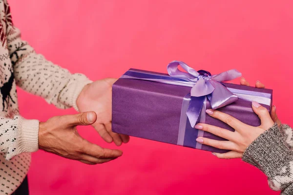 Image recadrée de petite amie donnant cadeau en boîte violette au petit ami isolé sur rose — Photo de stock