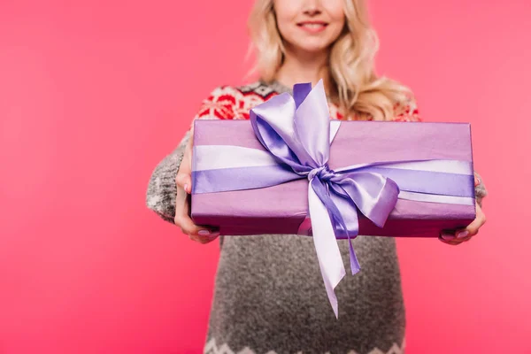 Imagem cortada de menina em suéter mostrando presente violeta isolado em rosa — Fotografia de Stock