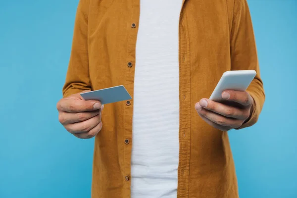 Imagen recortada del hombre que sostiene la tarjeta de crédito y el teléfono inteligente aislado en azul - foto de stock