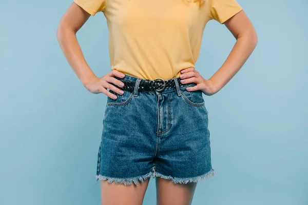 Cropped image of girl in shirt and shorts standing with hands akimbo isolated on blue — Stock Photo