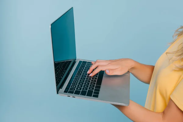 Обрізане зображення дівчини, що тримає ноутбук з порожнім екраном ізольовано на синьому — стокове фото