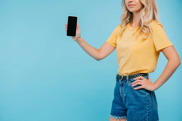 Image recadrée de fille en chemise et short tenant smartphone avec écran blanc isolé sur bleu — Photo de stock