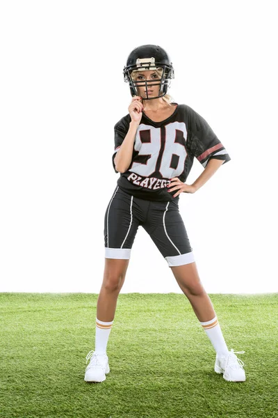 Спортивна молода жінка в американській футбольній формі стоїть на зеленій траві ізольована на білому — стокове фото