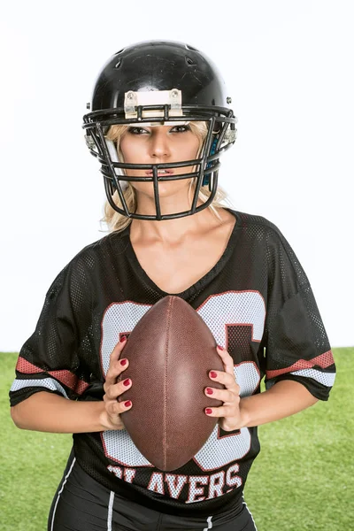 Sportliche junge Frau in American-Football-Uniform mit Ball blickt isoliert auf weiße Kamera — Stockfoto