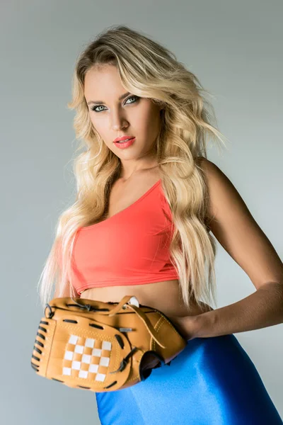 Крупним планом портрет привабливої молодої жінки в спортивному одязі з бейсбольною рукавичкою дивиться на камеру на сірому — стокове фото