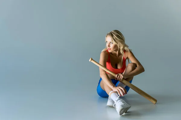 Fitte junge Frau mit Baseballschläger sitzt auf grau und schaut weg — Stockfoto