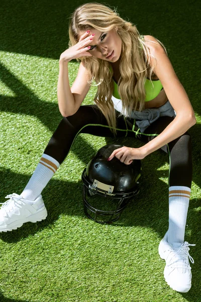 Vista aérea de la joven deportista sentada sobre hierba verde con casco de fútbol americano - foto de stock