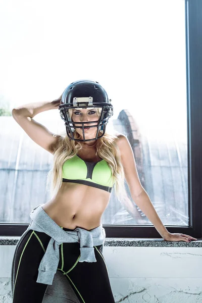 En forma de mujer joven en sujetador deportivo y casco de fútbol americano - foto de stock