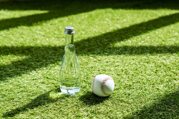 Glass water battle with baseball ball lying on green grass — Stock Photo