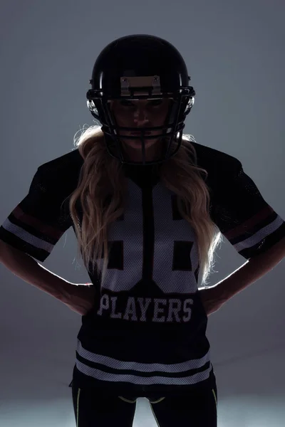 Silhouette sombre de jeune femme sportive en équipement de football américain sur gris — Photo de stock
