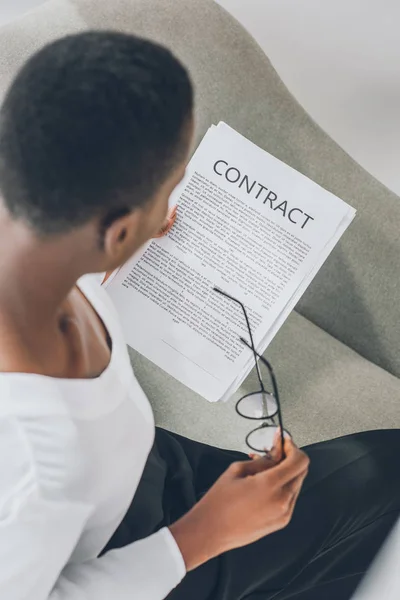 Hochwinkelaufnahme einer eleganten afrikanisch-amerikanischen Geschäftsfrau, die Vertrag liest und Brille im Büro hält — Stockfoto