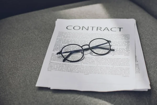 Brille und Geschäftsvertrag auf grauem Sessel im Büro — Stockfoto
