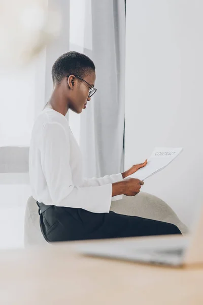 Vue latérale de élégante femme d'affaires afro-américaine attrayante lisant des documents au bureau — Photo de stock