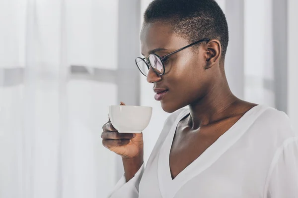 Side view of stylish attractive african american businesswoman drinking coffee in office — Stock Photo