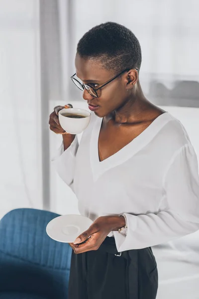 Elegante atractiva mujer de negocios afroamericana bebiendo café en la oficina - foto de stock