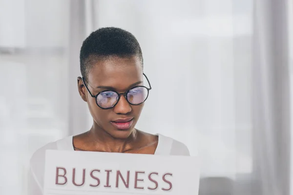 Retrato de mujer de negocios afroamericana en gafas leyendo periódico en la oficina - foto de stock
