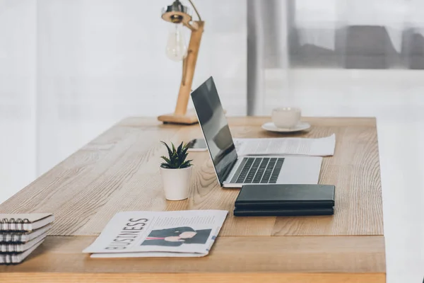 Бізнес-газета, ноутбук і блокноти на дерев'яному столі в офісі — Stock Photo