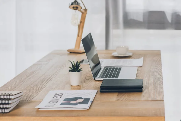 Periódico de negocios, portátil y cuadernos en la mesa de madera en la oficina — Stock Photo