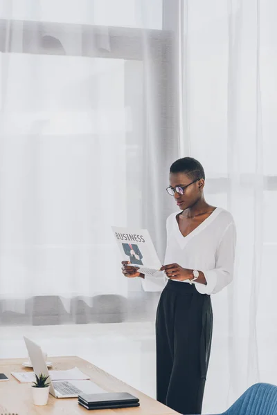Stylish attractive african american businesswoman with short hair reading newspaper in office — Stock Photo