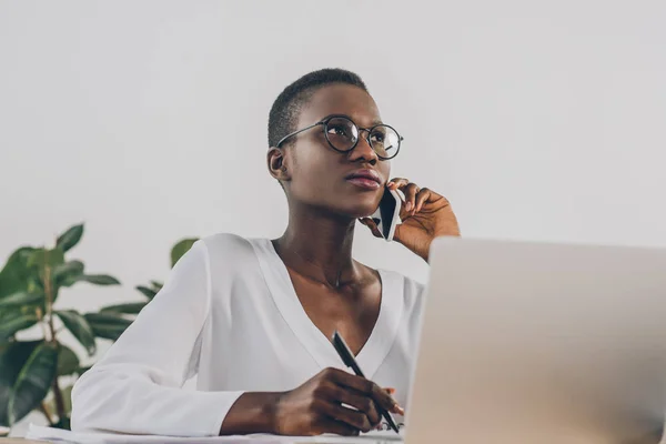 Elegante donna d'affari afro-americana attraente che parla con lo smartphone e distoglie lo sguardo in ufficio — Foto stock