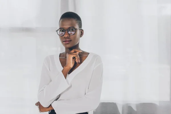 Pensativa mujer de negocios afroamericana elegante mirando a la cámara en la oficina - foto de stock