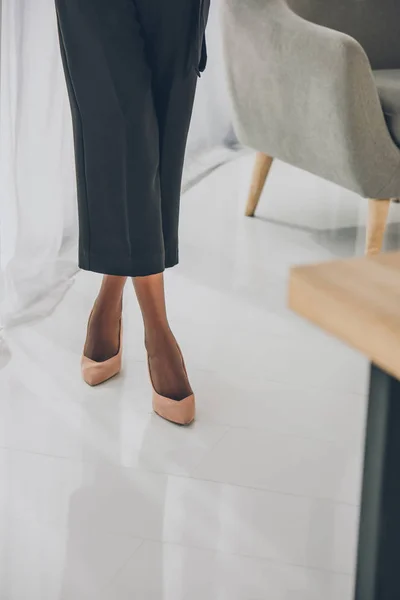 Imagem cortada de mulher de negócios americana africana elegante em saltos altos de pé no escritório — Fotografia de Stock