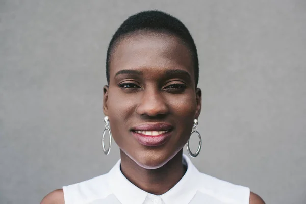 Porträt einer lächelnden attraktiven afrikanisch-amerikanischen Frau, die in die Kamera in der Nähe einer grauen Wand blickt — Stockfoto