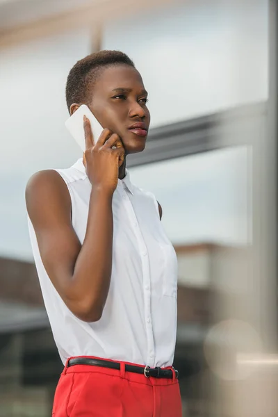 Vista laterale di elegante donna d'affari afro-americana attraente che parla con lo smartphone sulla strada — Foto stock