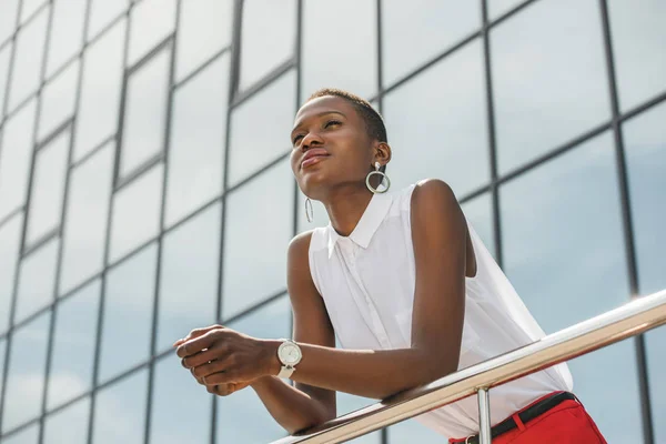 Низький кут зору стильна приваблива афроамериканська бізнес-леді, спираючись на перила поблизу бізнес-центру — стокове фото